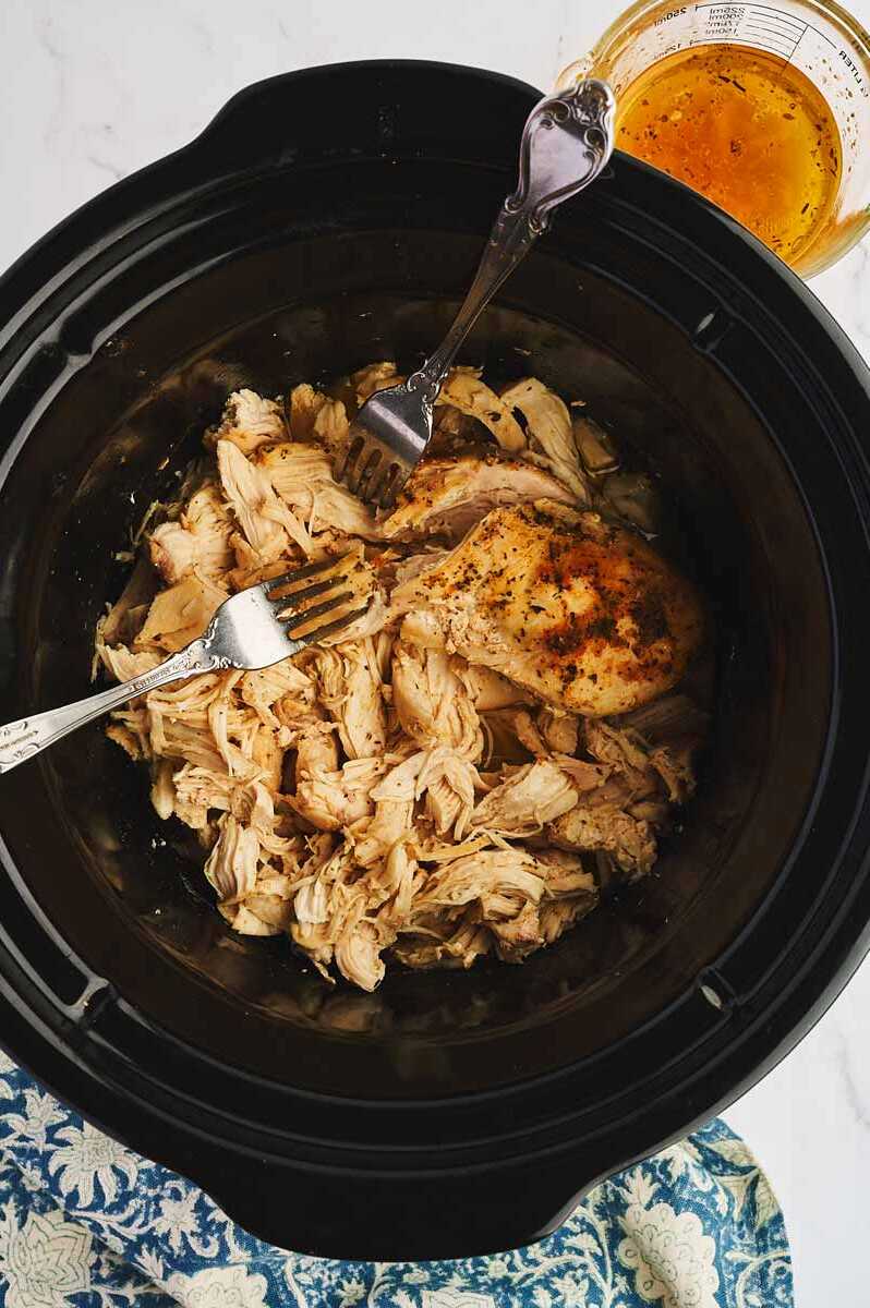 Shredding cooked chicken breast in a slow cooker.