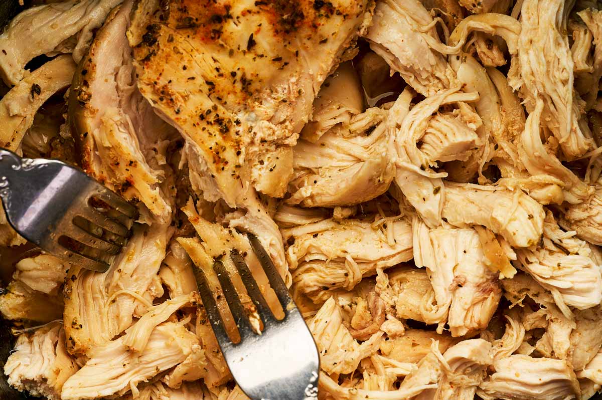 Close up photo of forks shredding chicken.