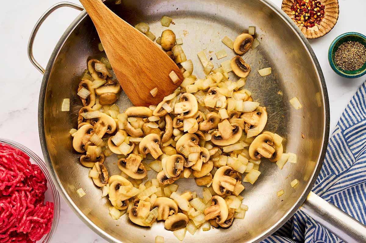 Sautéed onion and mushrooms in a stainless steel skillet.