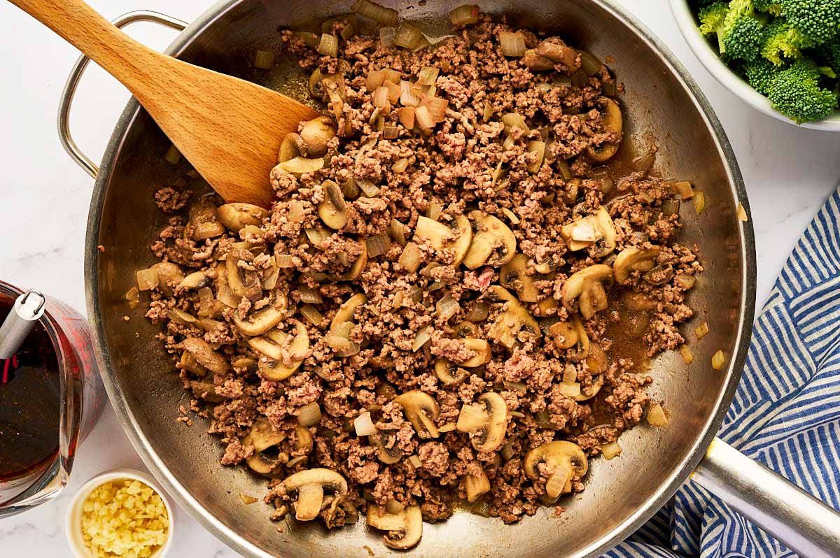 Sautéed onion and mushrooms in a stainless steel skillet with browned ground beef.