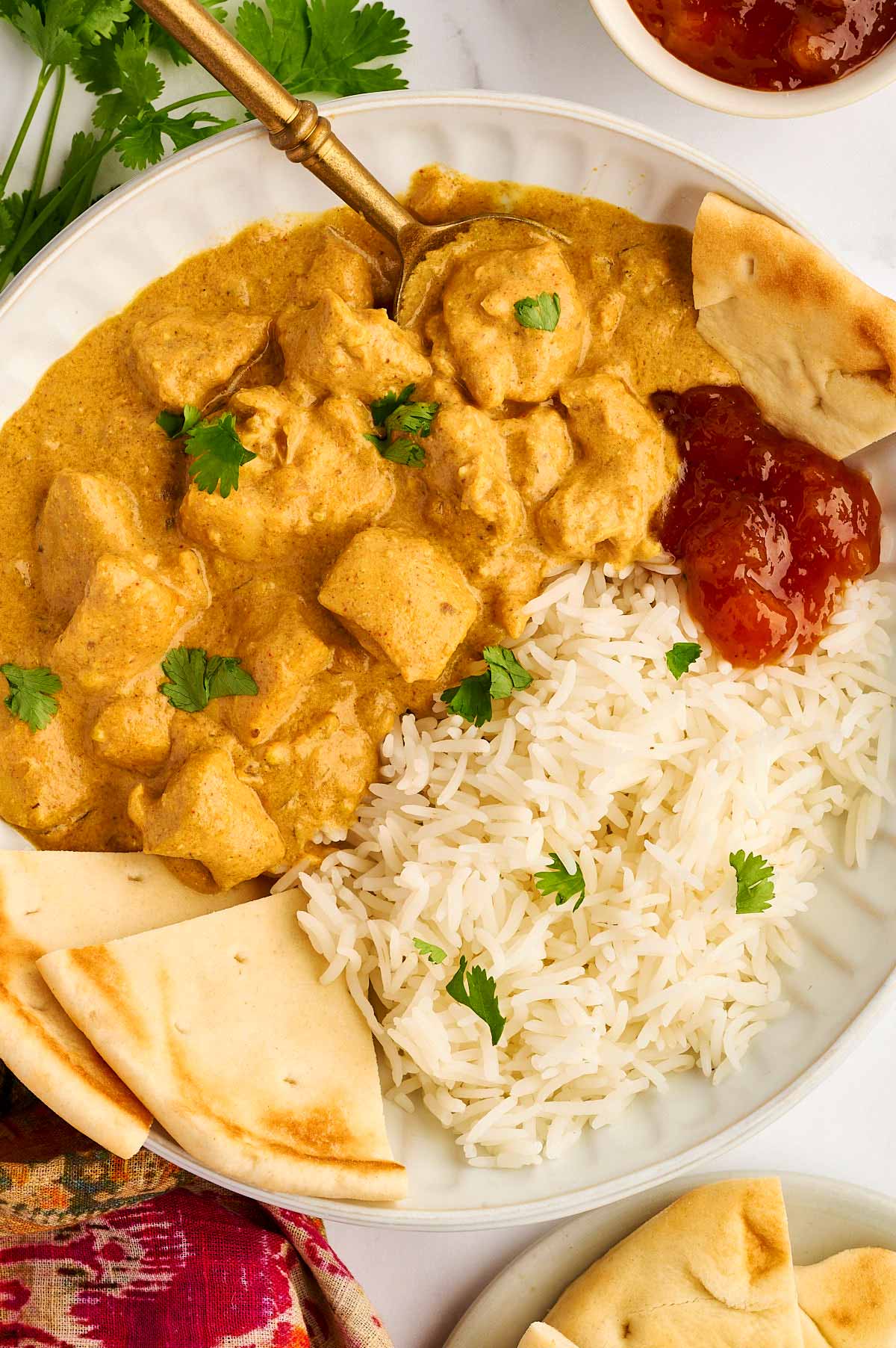 Overhead view of coconut chicken curry in a bowl with rice, mango chutney and flatbread.