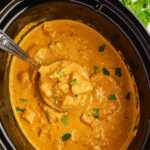 Overhead view of a black slow cooker with coconut chicken curry and a ladle.