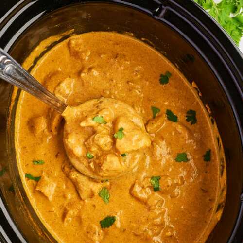 Overhead view of a black slow cooker with coconut chicken curry and a ladle.