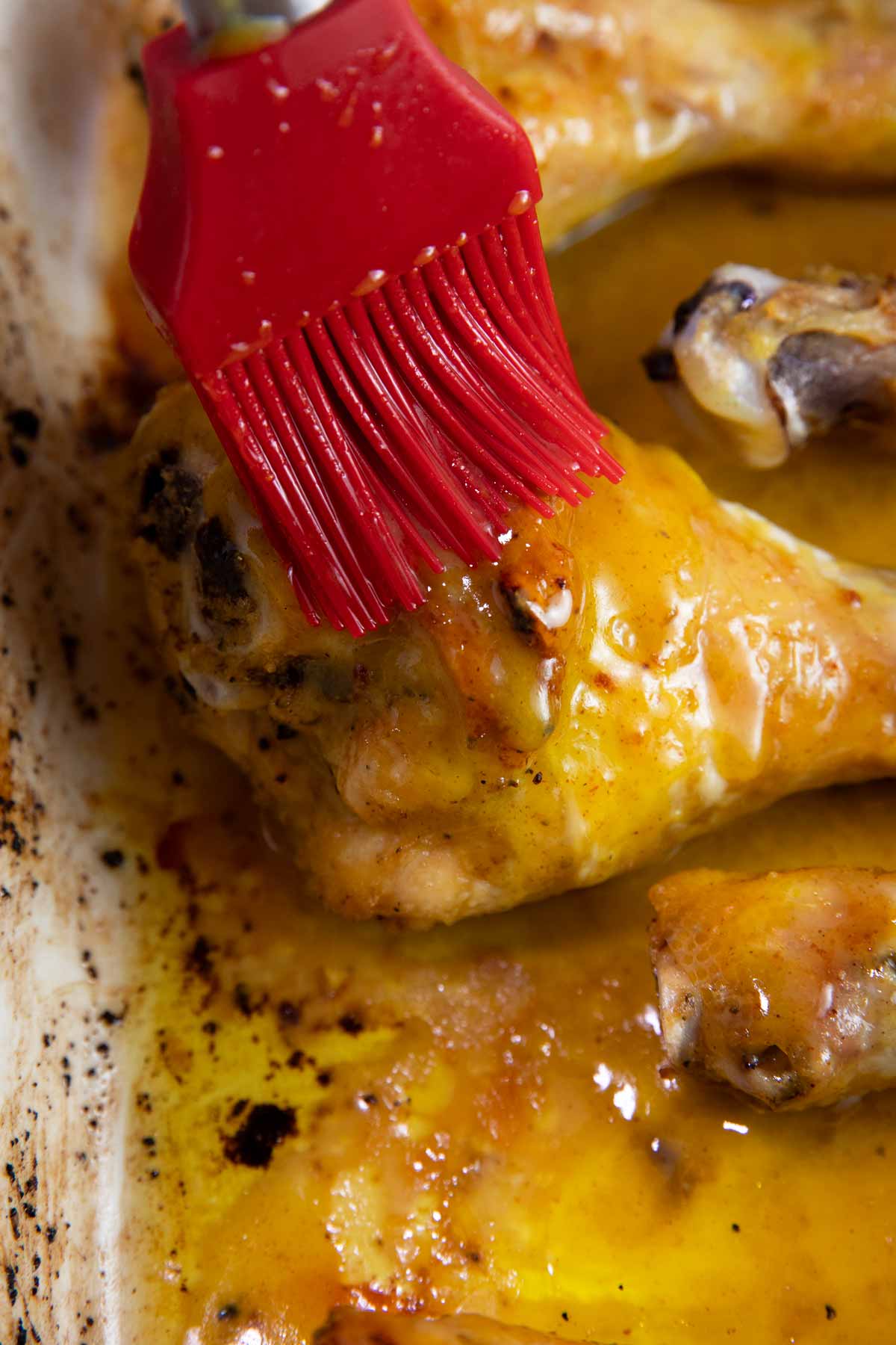 Red silicone brush brushing glaze onto a baked chicken leg.