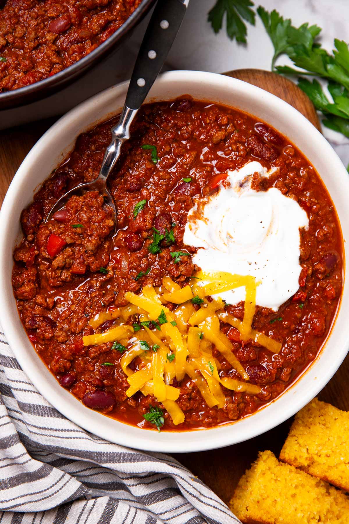 Bowl of chili with cheese, sour cream and cornbread on the side.