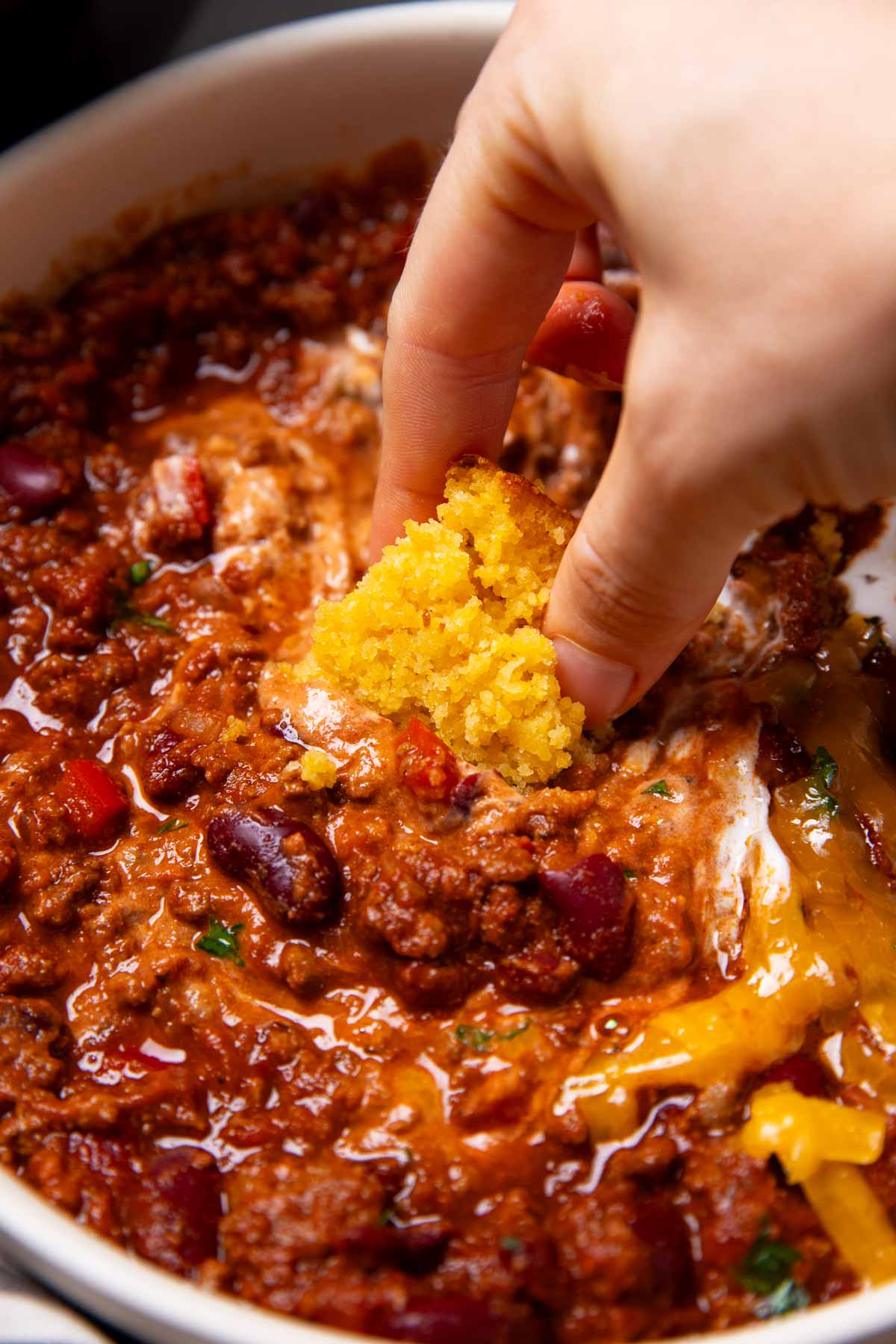 Hand dipping cornbread into bowl of chili.
