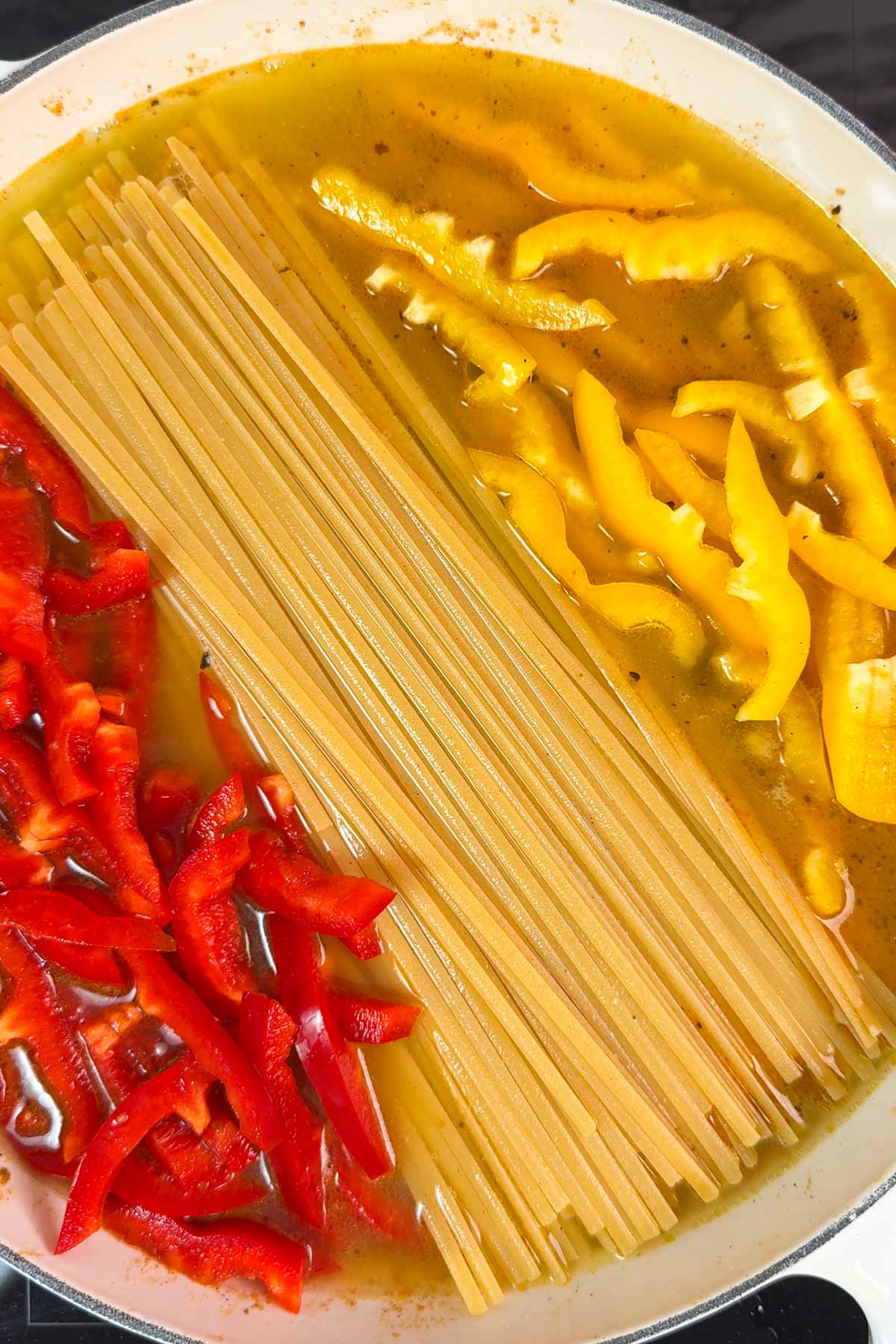 Uncooked linguine and sliced bell peppers in a pan.