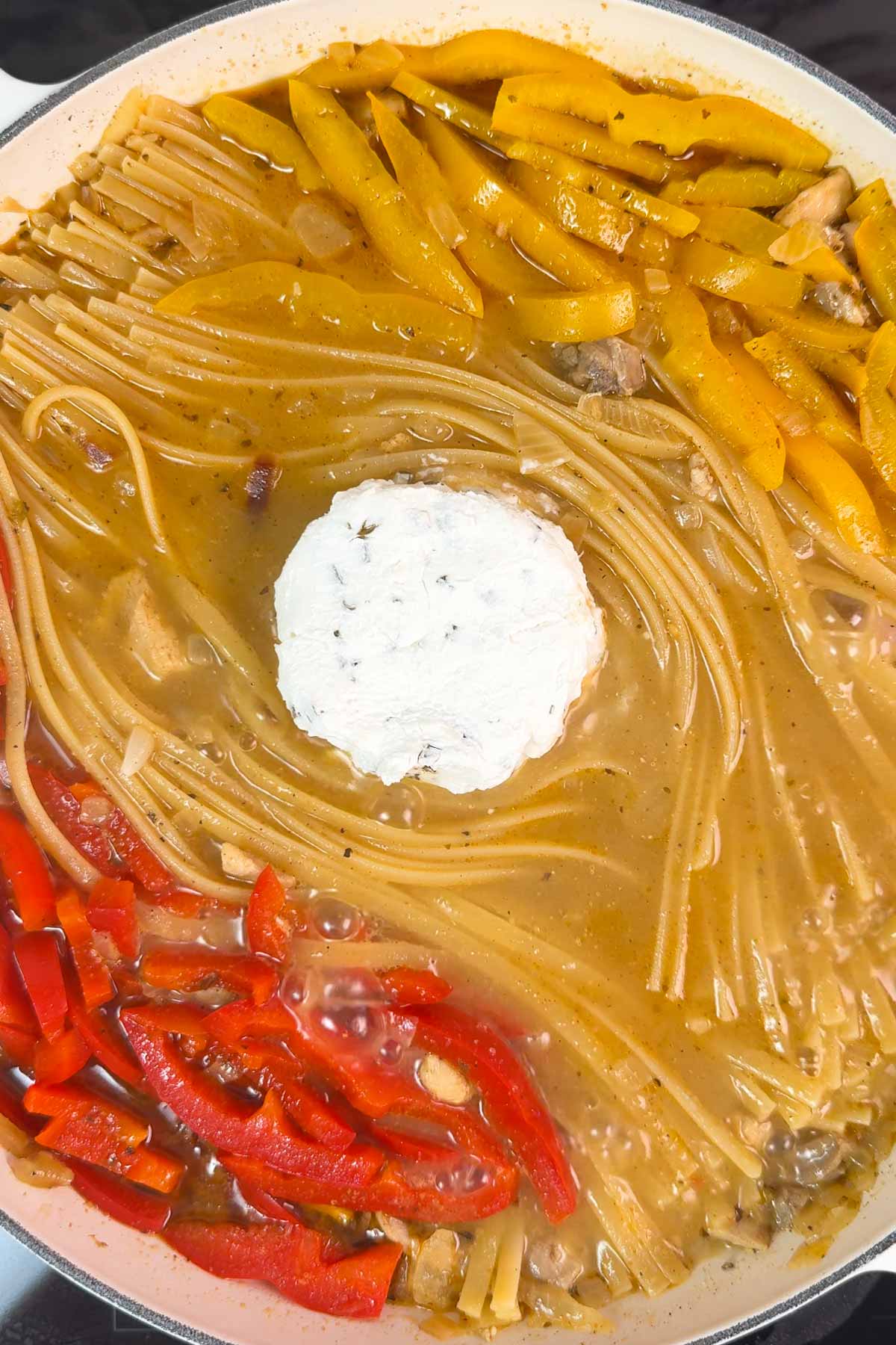Half cooked linguine and sliced bell peppers in a pan with Boursin cheese.