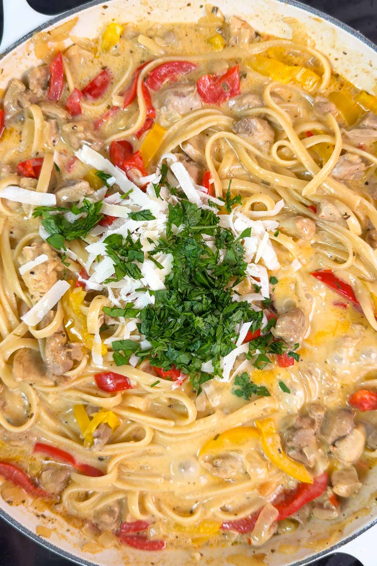Creamy Cajun Chicken Pasta in a pan with shredded parmesan cheese and chopped parsley.
