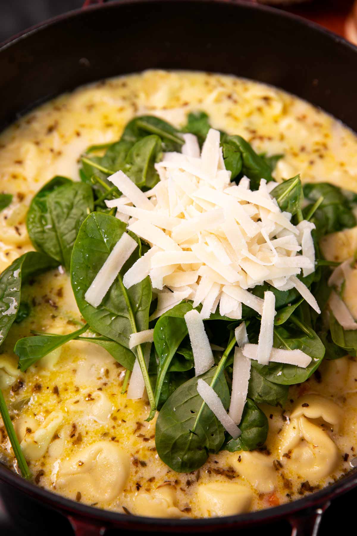 Spinach and shredded parmesan on top of creamy tortellini and chicken soup.