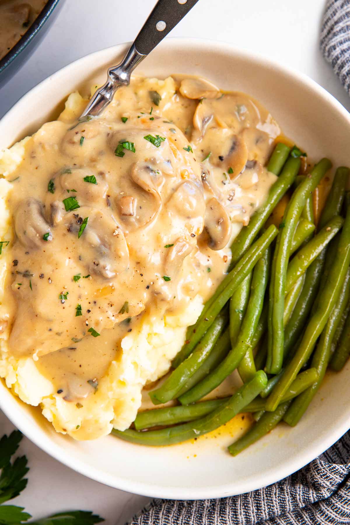Plate with creamy mushroom chicken over mashed potatoes with green beans.