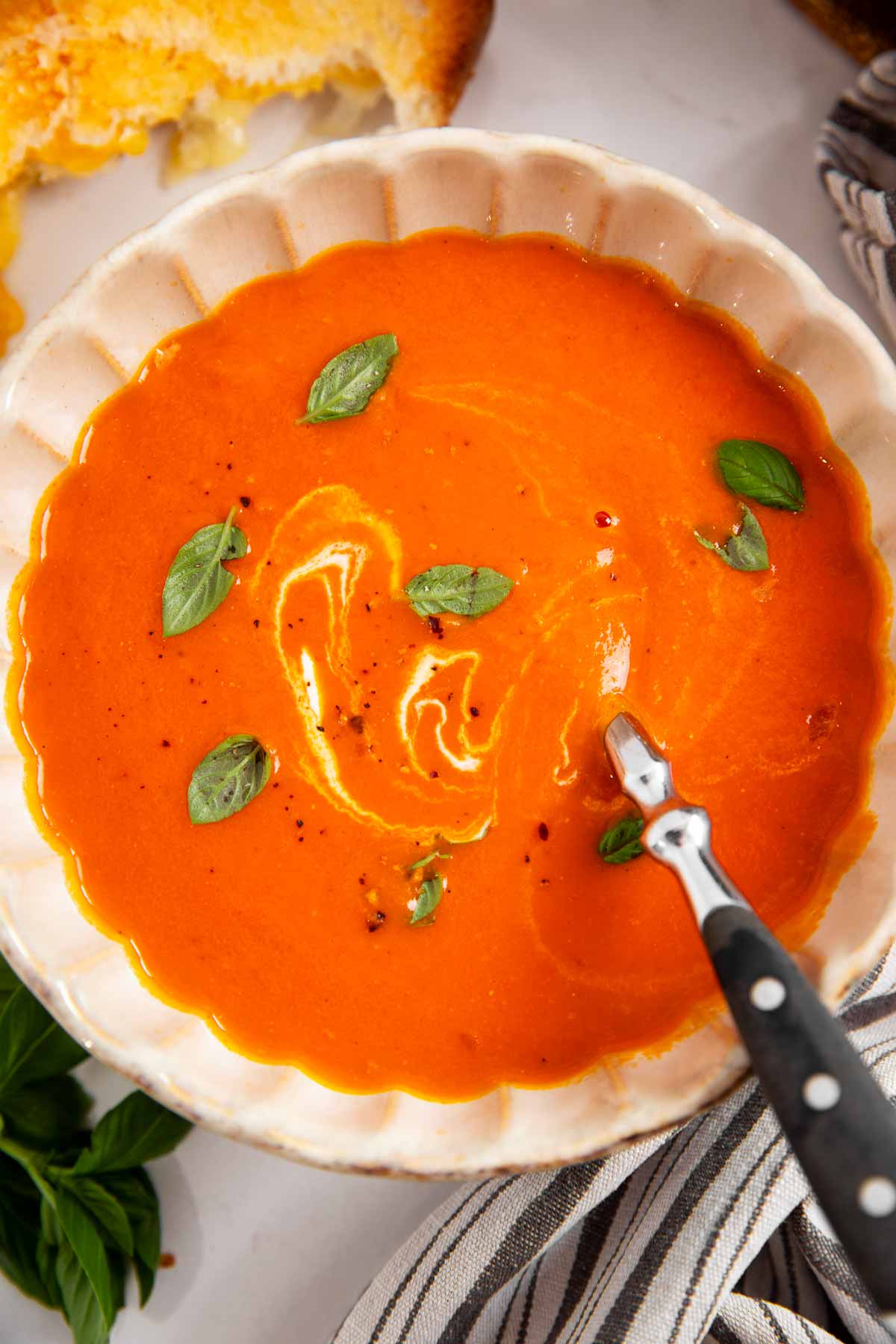 Overhead view of a bowl of tomato soup being served with grilled cheese.