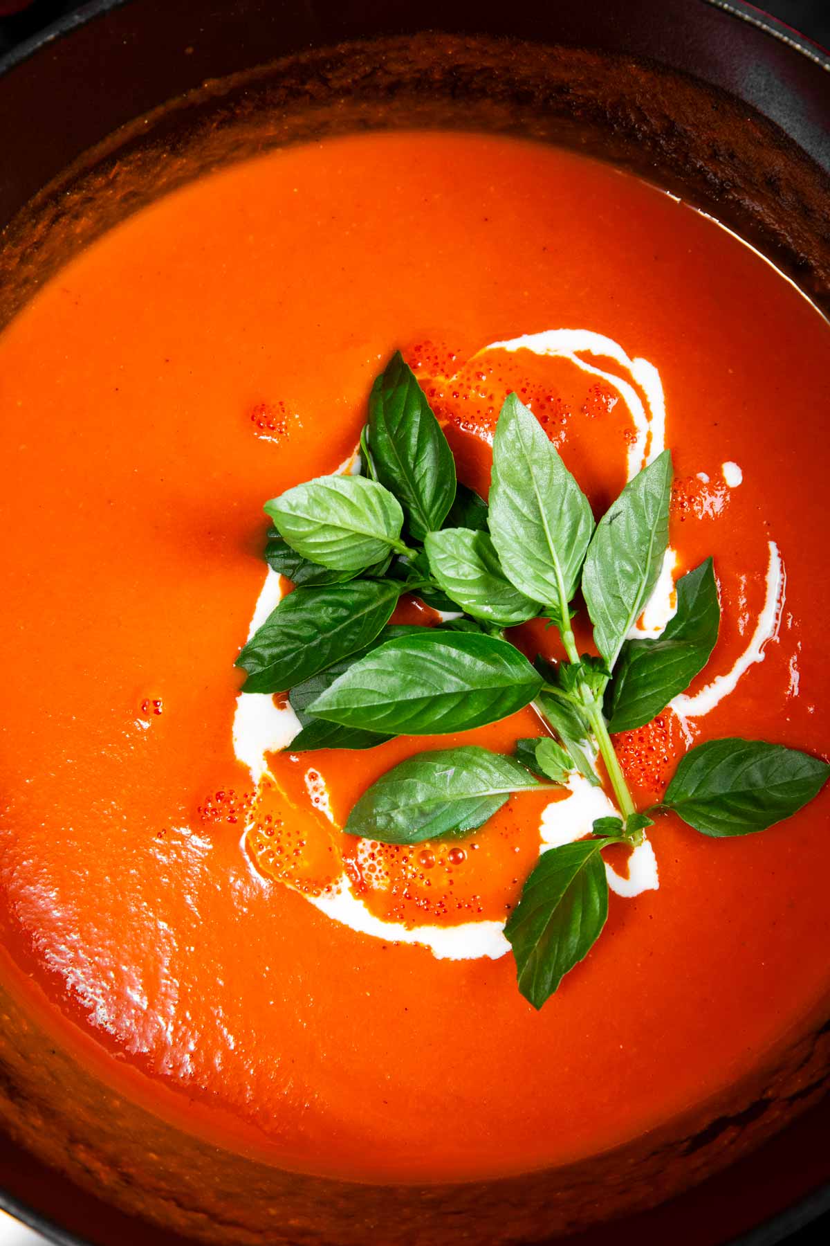 Tomato soup in pot with cream and fresh basil.