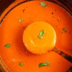 Close up photo of a ladle scooping tomato soup from a pot.