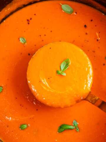Close up photo of a ladle scooping tomato soup from a pot.