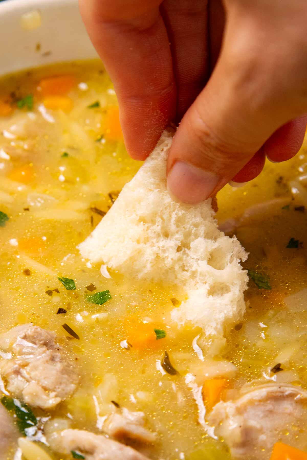 Dipping bread in a bowl of Lemon Chicken Orzo Soup.