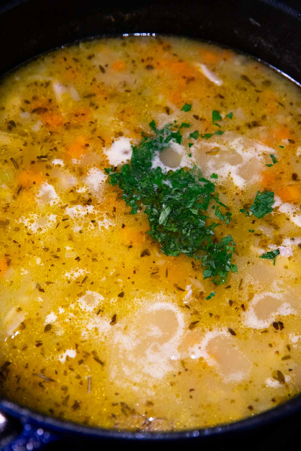 Chopped parsley on top of lemon chicken orzo soup in a cast iron pot.