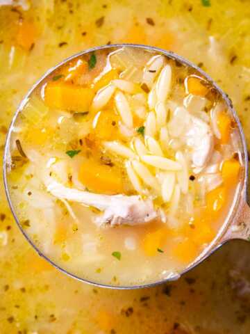 Close up of a ladle with lemon chicken orzo soup.