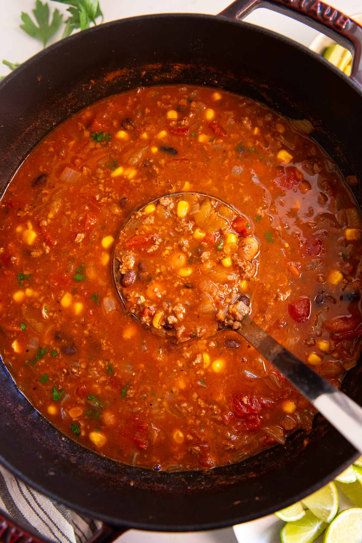 Ladle scooping taco soup from a cast iron pot.