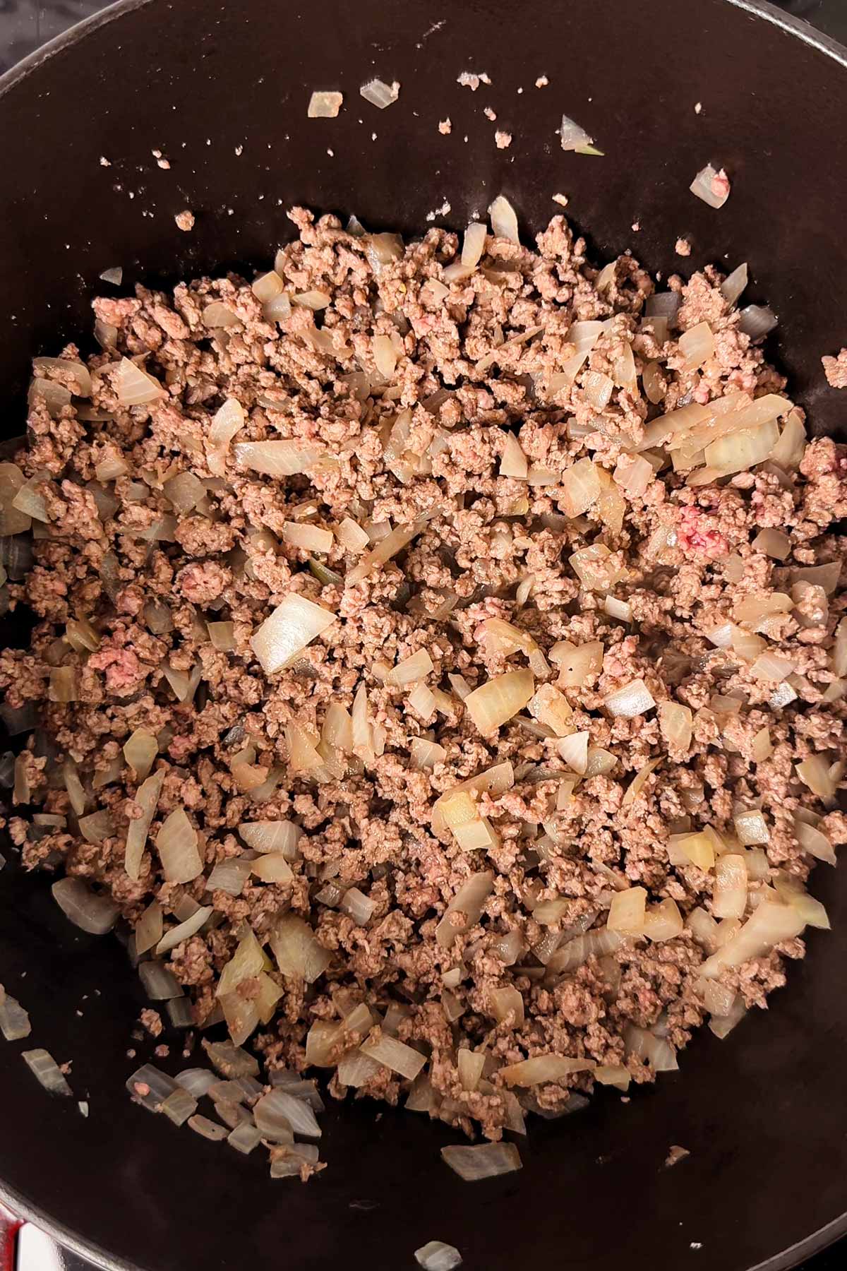 Sautéed onion and browned ground beef in a cast iron pot.