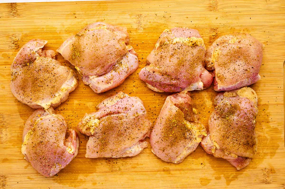Seasoned chicken thighs on a wooden board.