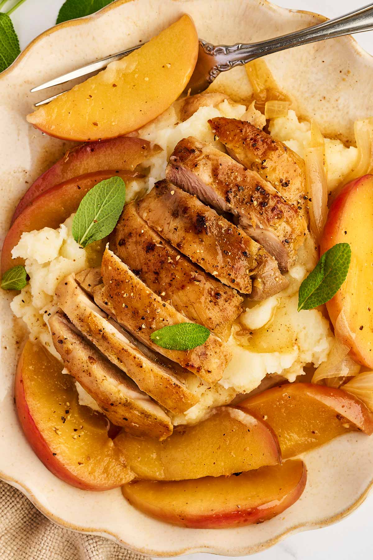 Sliced chicken thigh on mashed potatoes with apple slices.