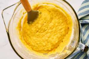 Folding cornbread batter in a glass bowl.
