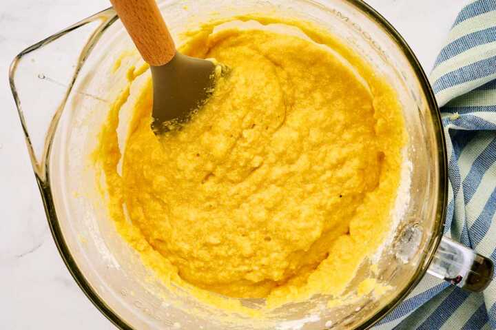 Folding cornbread batter in a glass bowl.