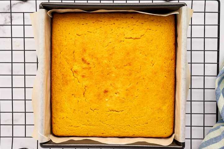 Baked cornbread in a metal pan on a cooling rack.