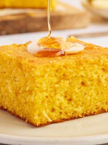 Honey drizzling over cornbread from a wooden honey spoon.