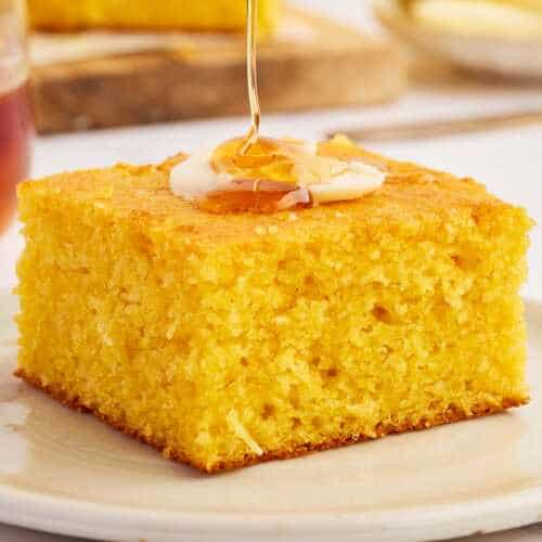 Honey drizzling over cornbread from a wooden honey spoon.