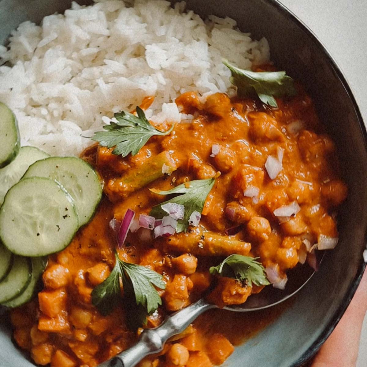 Human hand holding a bowl filled with rice and sweet potato chickpea curry.